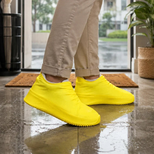 A person wearing khaki pants and bright yellow silicone shoe covers stands on a wet tiled floor near a doorway.