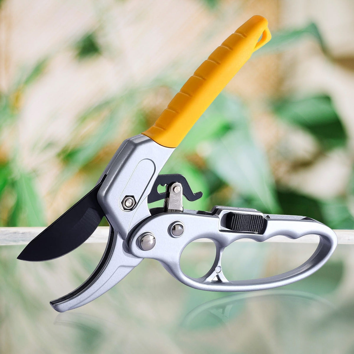 Silver and yellow pruning shears with black blades against a blurred green background.