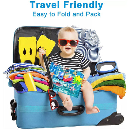 A baby in sunglasses sits in an open blue suitcase, holding a folded water mat, surrounded by travel items.