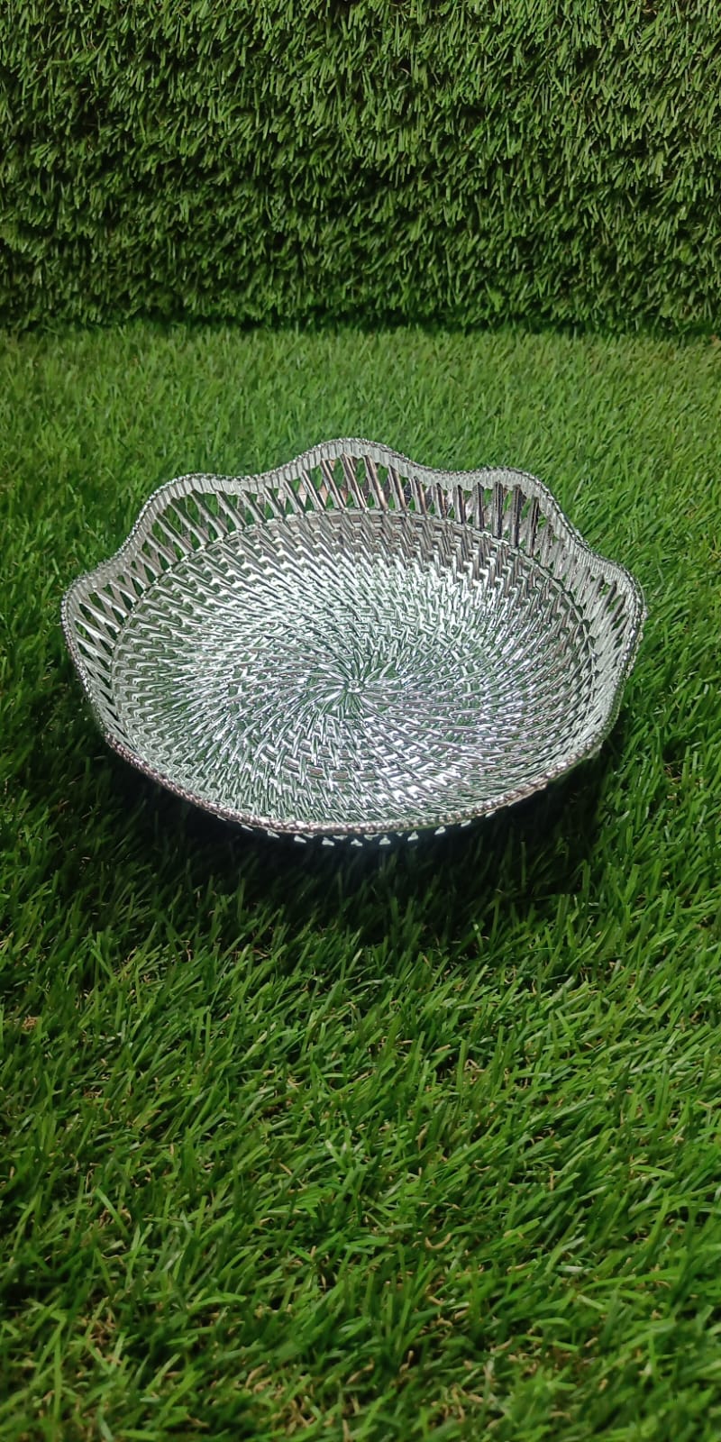 A silver plastic scalloped serving bowl with a textured bottom sits on a vibrant green artificial grass surface.
