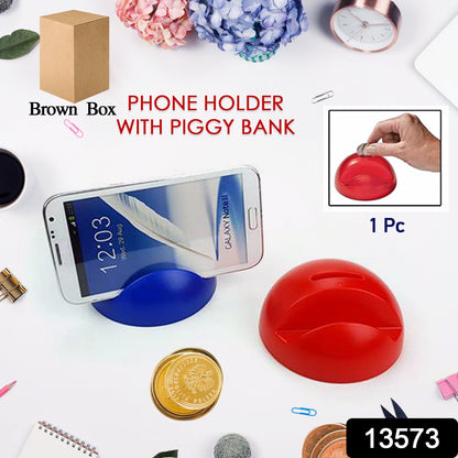 A blue phone holder with a phone and a red piggy bank with coins on a white desk with office supplies.