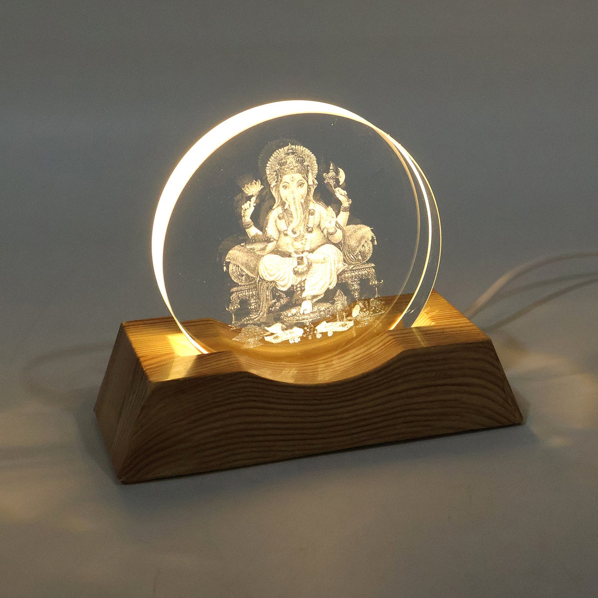 The Ganesha 3D illusion lamp with a clear acrylic panel and wooden base, brightly illuminated.