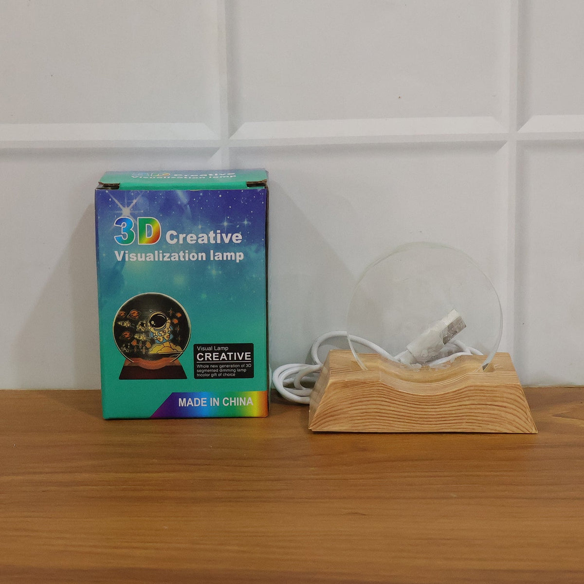Product box for a 3D creative visualization lamp next to the unlit Ganesha lamp on a wooden surface.