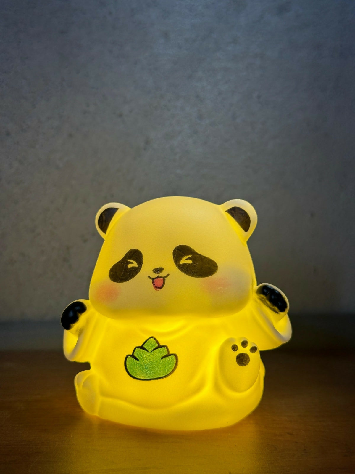 The panda night light glows brightly with a warm yellow light, highlighting its black and green details against a dark,