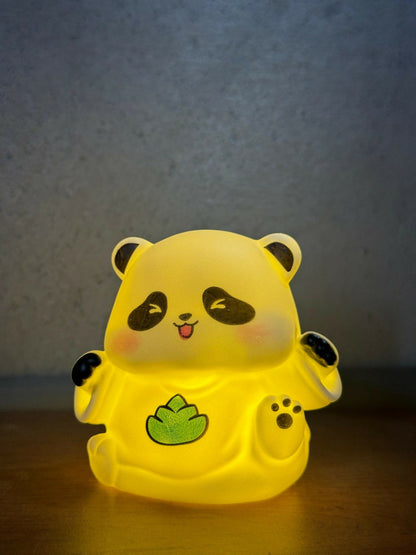 The panda night light glows brightly with a warm yellow light, highlighting its black and green details against a dark,