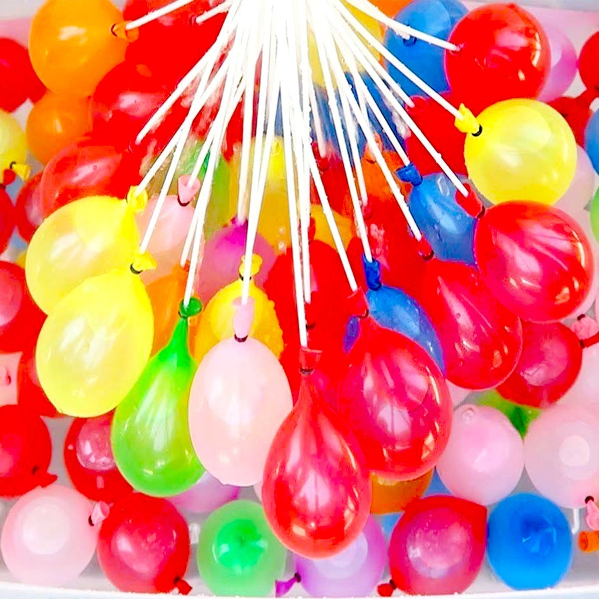 Close-up of numerous colorful water balloons, some filled, with white filling straws.