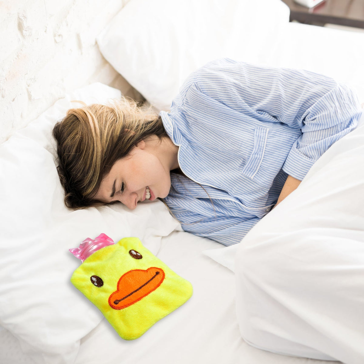 A woman lying in bed, appearing to be in pain, with the yellow duck hot water bottle placed on her abdomen.