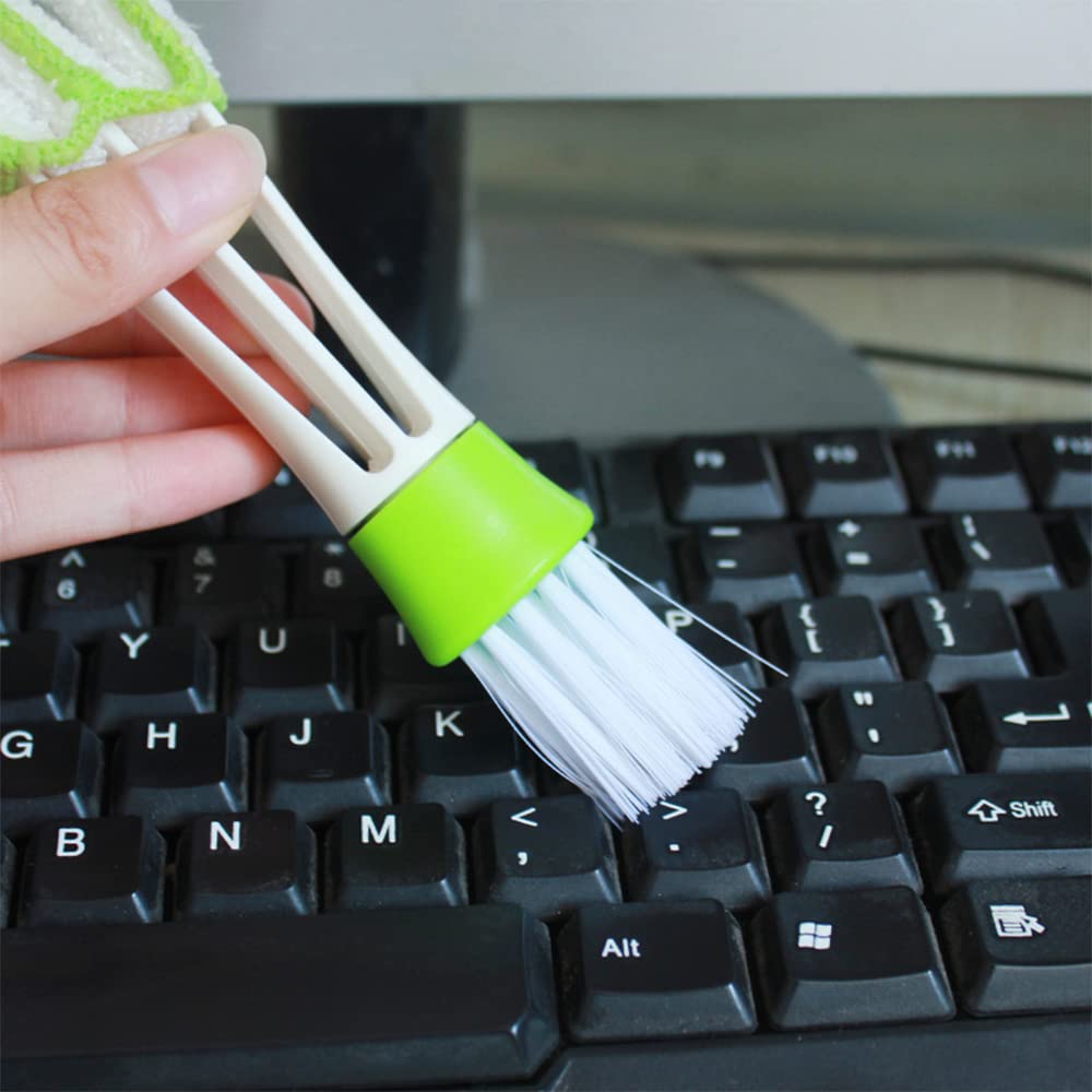 A hand holding a white and green 3-in-1 cleaning brush, using the brush head to clean a black keyboard.