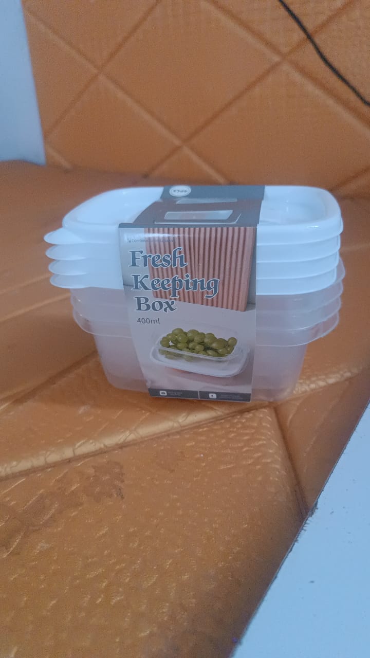 A stack of five clear plastic food containers with white lids, with a 'Fresh Keeping Box' label, on a brown textured surface.