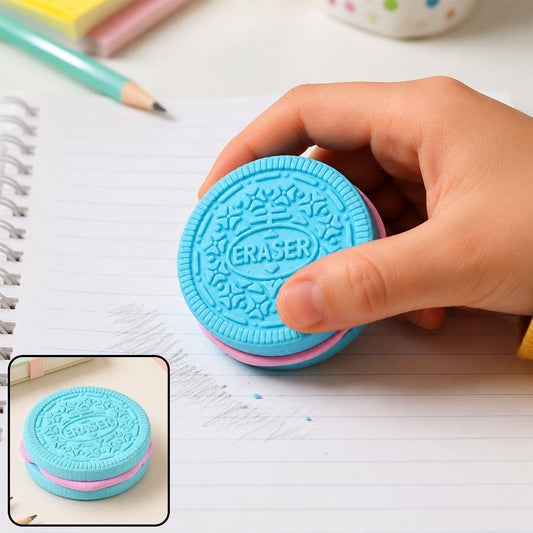 A hand holds a blue and pink cookie-shaped eraser on a lined notebook page, erasing a pencil mark.