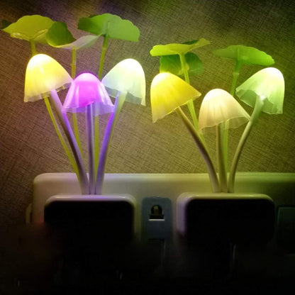 Two mushroom night lights with glowing colorful caps and green leaves are plugged into a wall outlet in a dim room.