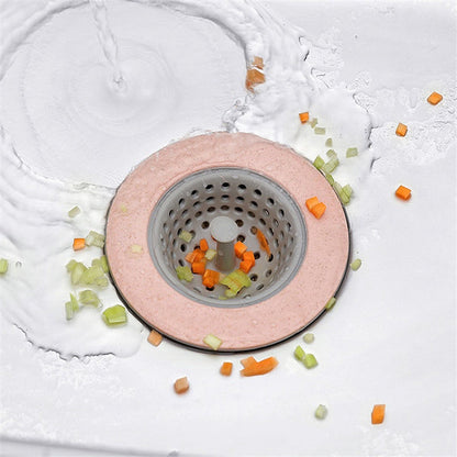 A pink and grey silicone sink strainer basket in a sink with water and chopped vegetables swirling around it.