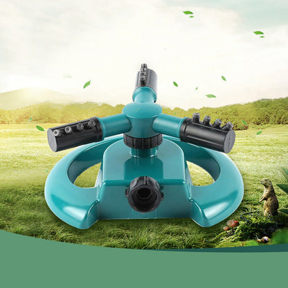 A teal and black garden sprinkler sits on a green field with a blurred natural background.