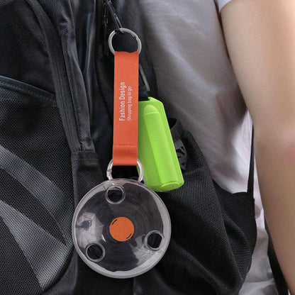 A close-up of an orange reusable bag dispenser with a black bag inside, clipped to a backpack strap.