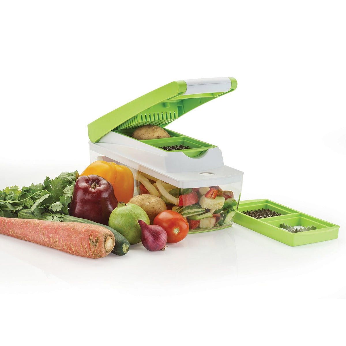 A green and white vegetable dicer is open, ready to chop a potato, surrounded by various whole and chopped vegetables.
