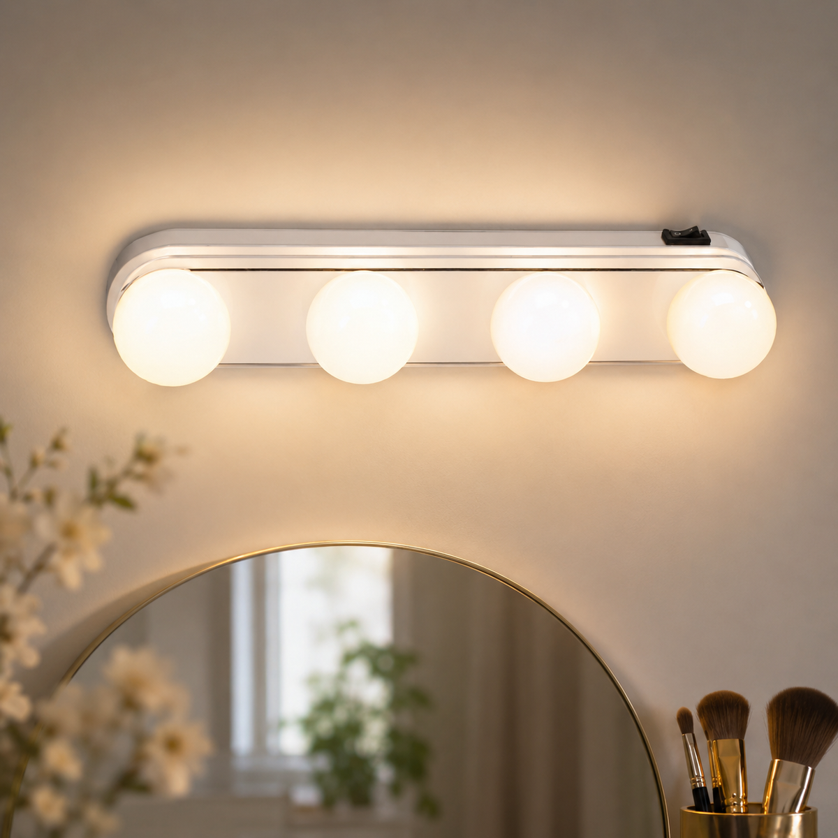 A white LED vanity light with four round bulbs is mounted above a gold-rimmed mirror, with flowers and brushes in the