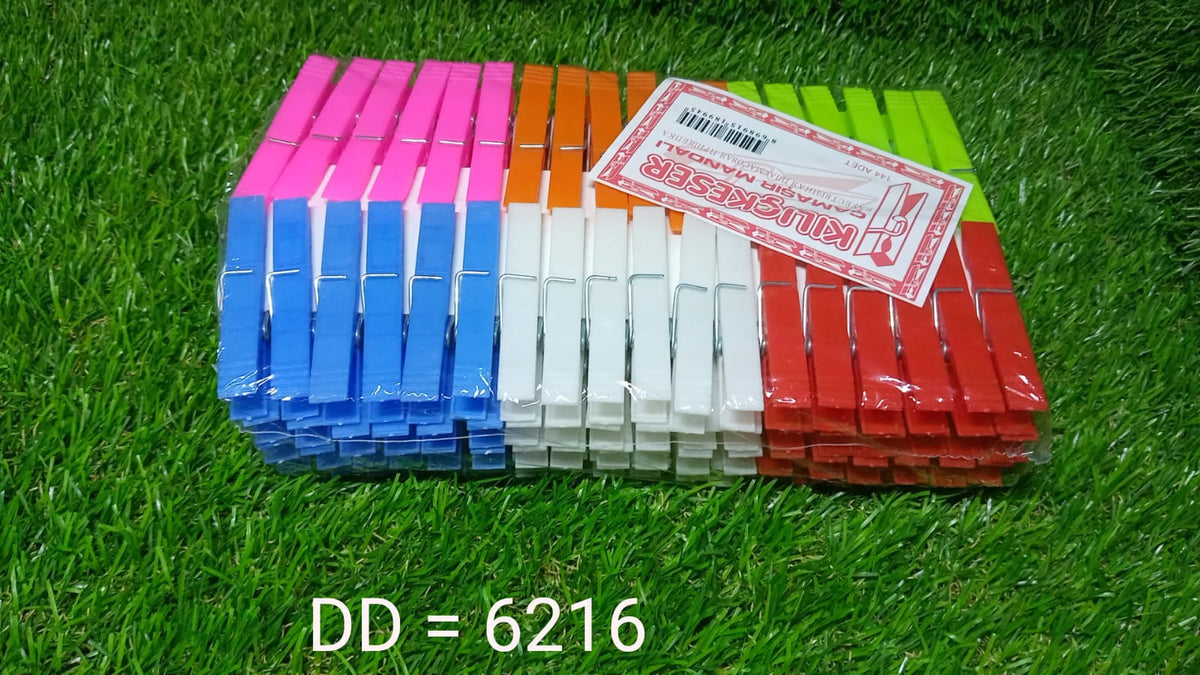 A large stack of colorful plastic clothes clips with a white label on top, resting on a vibrant green grass surface.