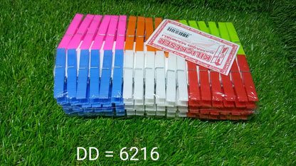 A large stack of colorful plastic clothes clips with a white label on top, resting on a vibrant green grass surface.
