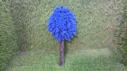 Blue microfiber duster with a black handle standing upright on a green artificial grass background.