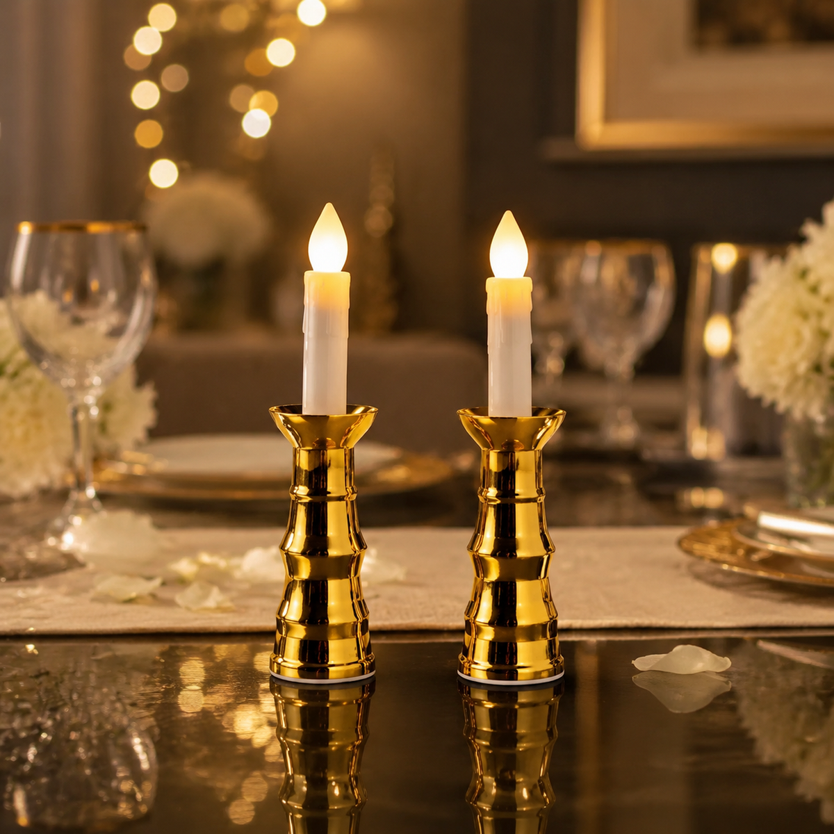 Two gold-based LED candles illuminate a dining table set with wine glasses and white flowers.