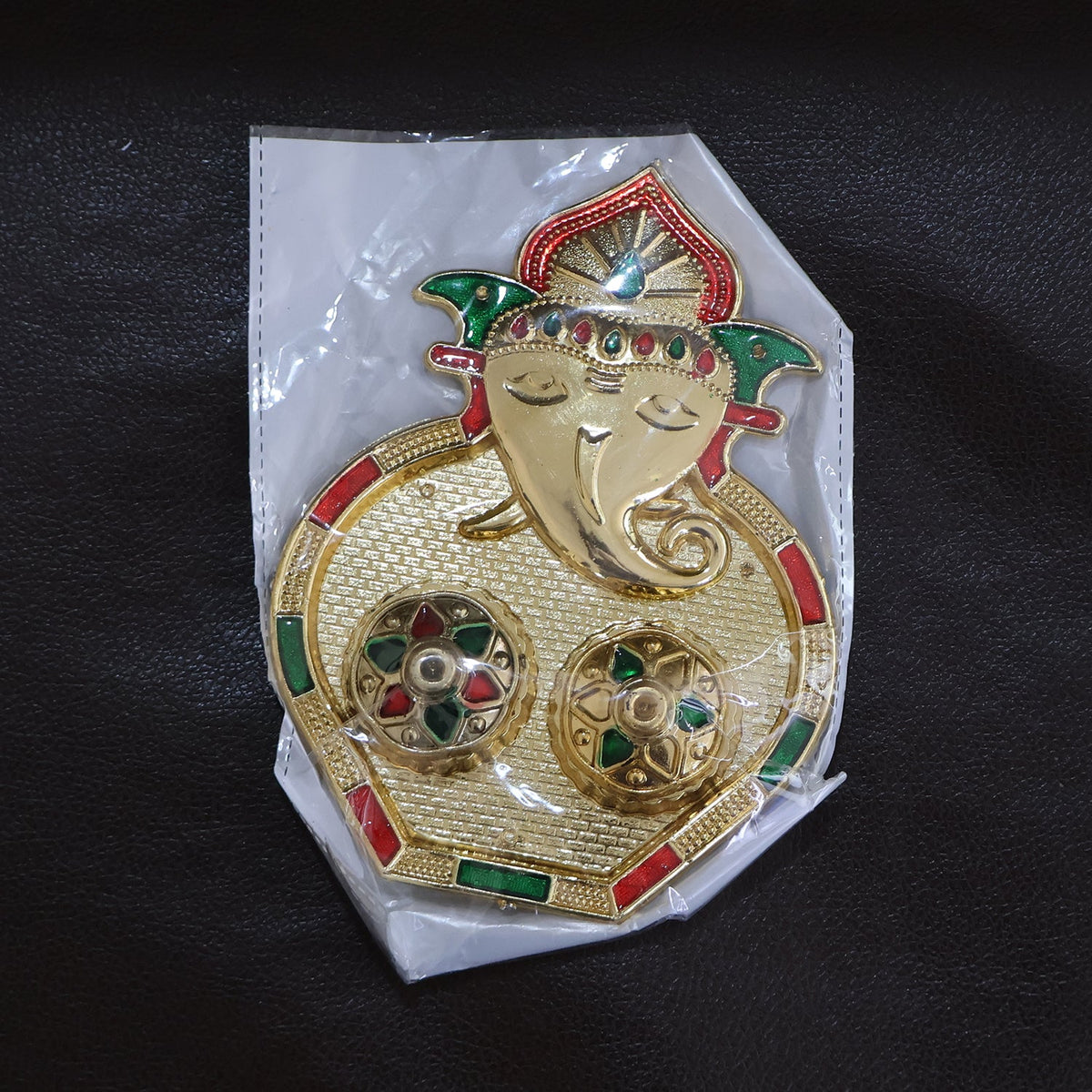 A golden Ganesh pooja thali with two small round containers, accented with red and green enamel details, sealed in clear