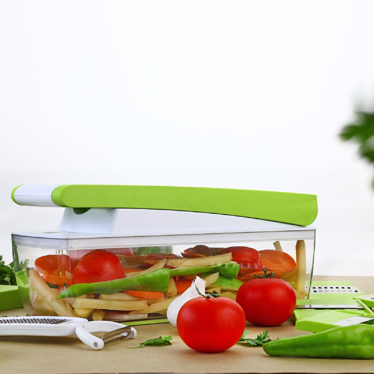 A green and white vegetable dicer sits on a wooden surface, filled with chopped vegetables, alongside whole tomatoes,