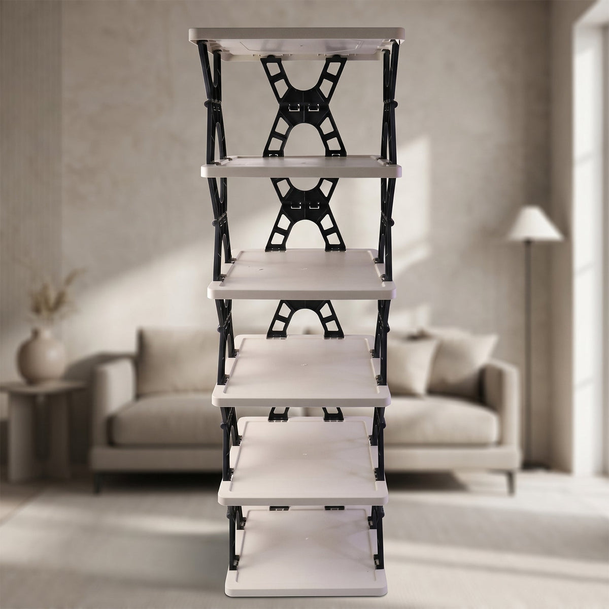 A front view of the light grey and black foldable shoe rack, empty, in a softly lit room with a couch.