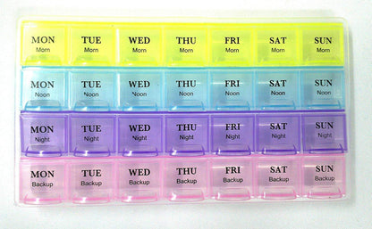 A close-up of the 28-slot, rainbow-colored pill organizer, showing day and time labels on each compartment.