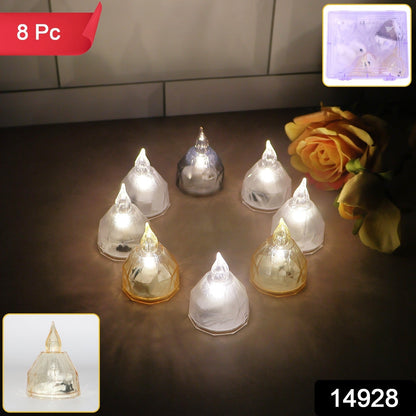 Eight LED diyas, some clear and some amber, glowing on a light brown surface with a rose and packaging visible.