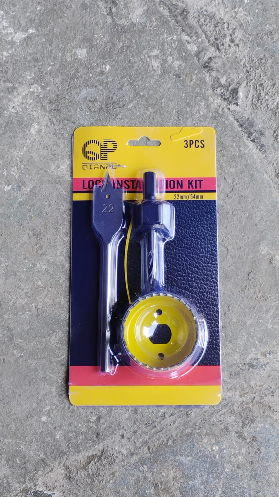 A yellow and black door lock installation kit with three pieces is packaged in a clear plastic blister pack.