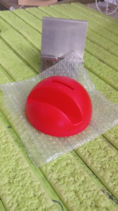 A red phone holder piggy bank wrapped in bubble wrap on a textured green surface with a metal stand.