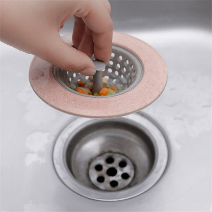 A hand lifting a pink and gray silicone sink strainer basket filled with chopped vegetables from a stainless steel sink.