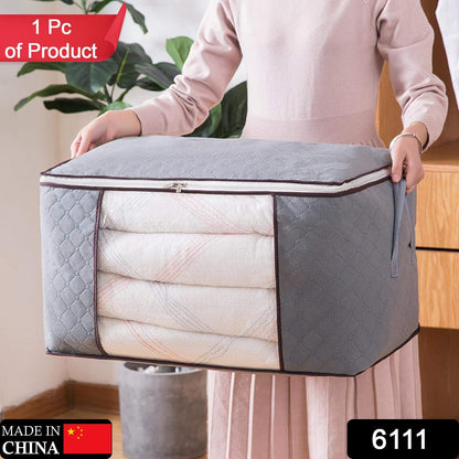 A person holds a grey quilted fabric storage bag with a clear window, filled with folded white blankets.