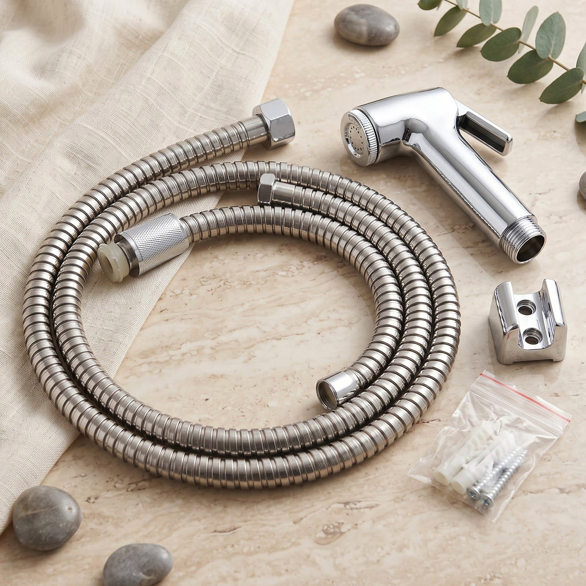 A coiled stainless steel hose, chrome bidet sprayer, wall mount, and screws on a light fabric and stone surface.