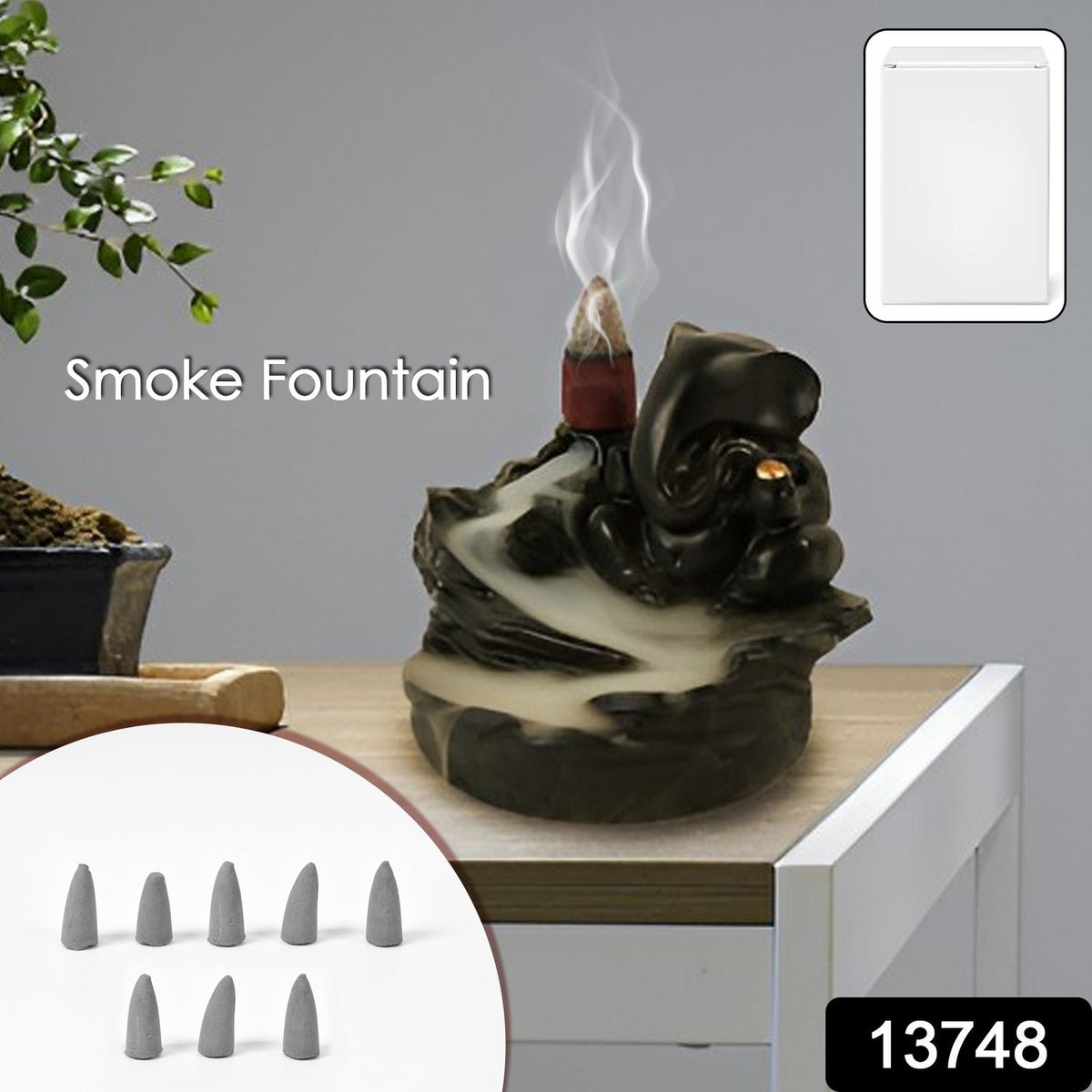Black Ganesha smoke fountain with smoke rising from a lit cone, shown with a small bonsai tree and a set of eight gray