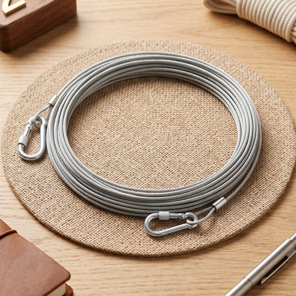A coiled silver stainless steel wire rope with two carabiner hooks rests on a round woven mat.