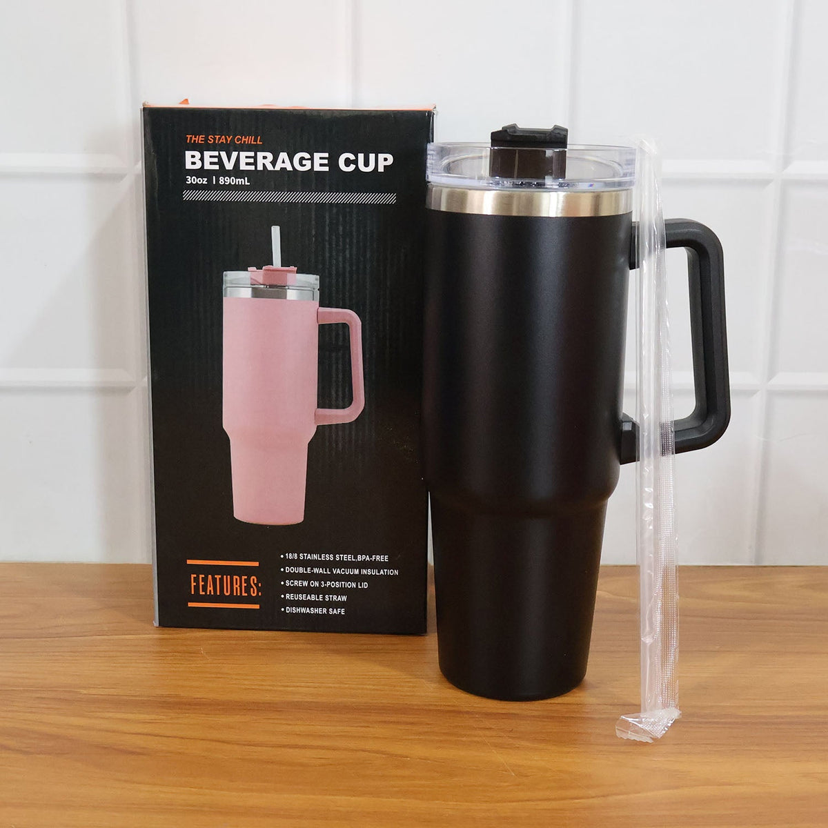 Black insulated travel mug with handle, lid, and straw next to its product box featuring a pink version of the mug.