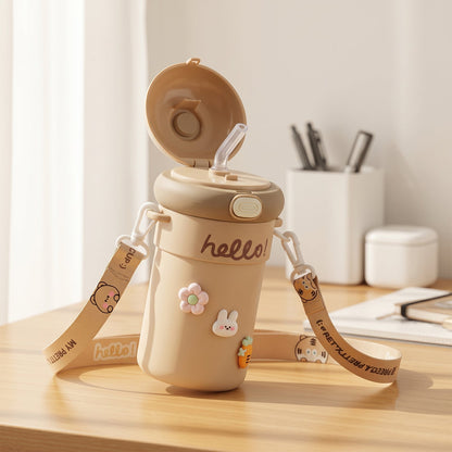 An open tan sipper bottle with a straw, 'hello!' inscription, and cute animal and flower charms, with a patterned strap, on