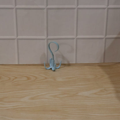 A light blue rotating multi-hook hanger sits on a light wooden surface against a white tiled wall.