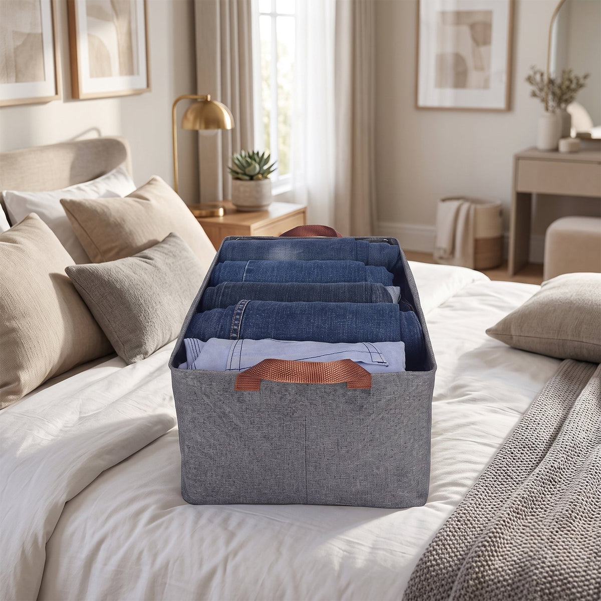 A gray foldable fabric storage basket filled with folded clothes on a bed in a bedroom setting.