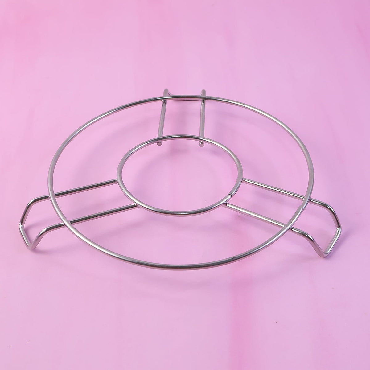 A silver wire hot pot stand is placed on a solid pink background.