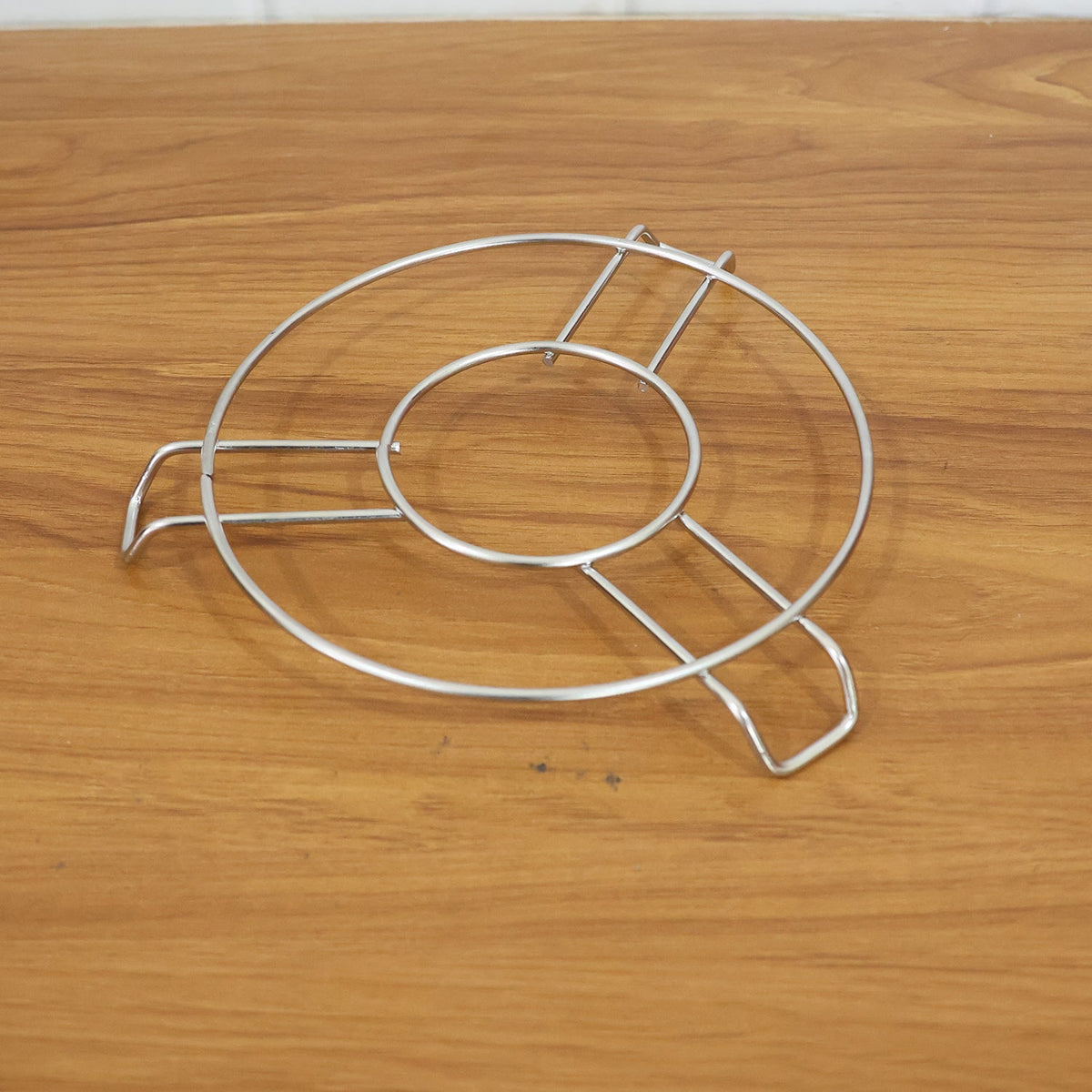 A silver wire hot pot stand is positioned on a light brown wooden table.