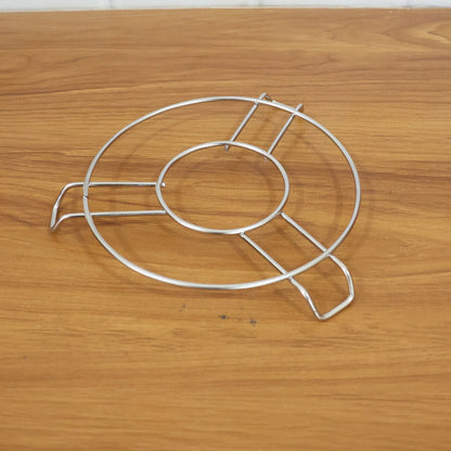 A silver wire hot pot stand is positioned on a light brown wooden table.