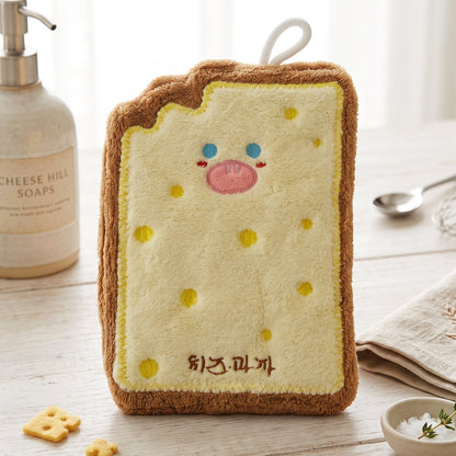 A cartoon cheese toast-shaped microfiber towel stands upright on a wooden counter next to a soap dispenser and small bowl.