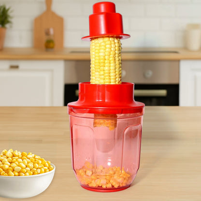 A red plastic corn kernel remover is in use on a wooden kitchen counter, with a cob being pressed through and kernels