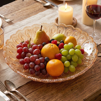 Amber glass platter with a peacock feather pattern, filled with various fresh fruits on a dining table with a lit candle and