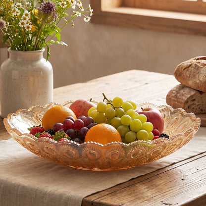 Amber glass platter filled with colorful fruits on a rustic wooden table, next to a vase of wildflowers and bread.