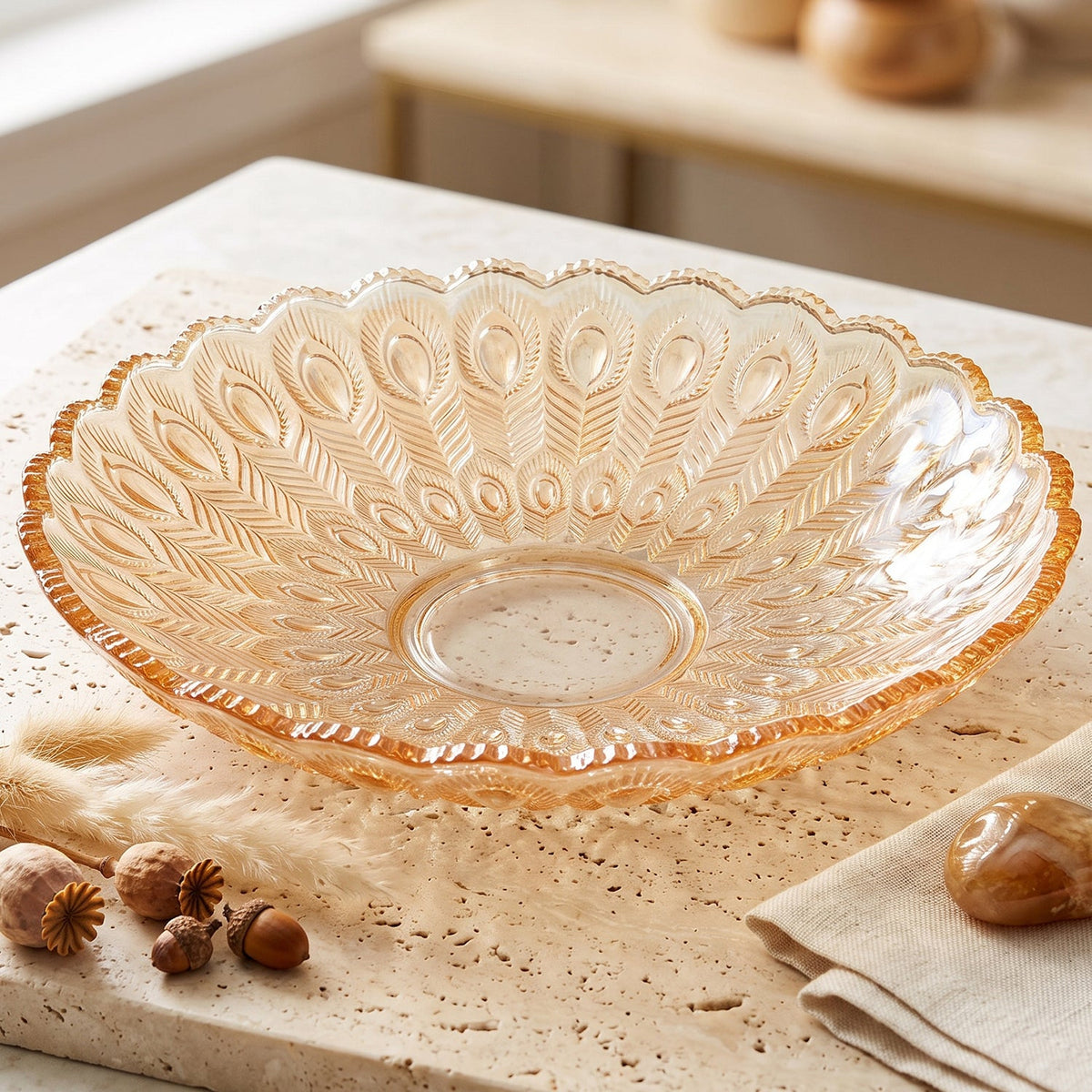 Empty amber glass platter with a feather design, resting on a textured stone surface with decorative nuts and a linen napkin.