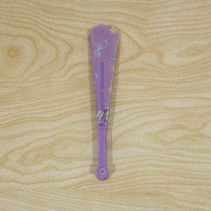 A closed purple folding hand fan with a subtle cat and bow pattern lies vertically on a light wooden surface.