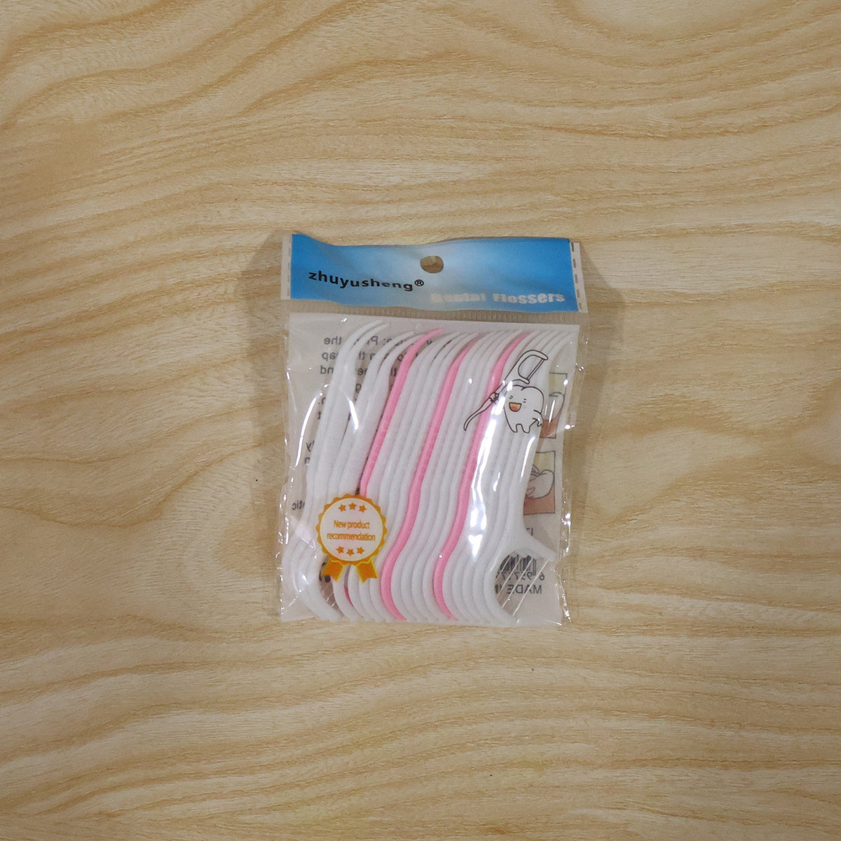 A clear plastic package of pink and white dental floss picks with a blue header, on a light wooden background.